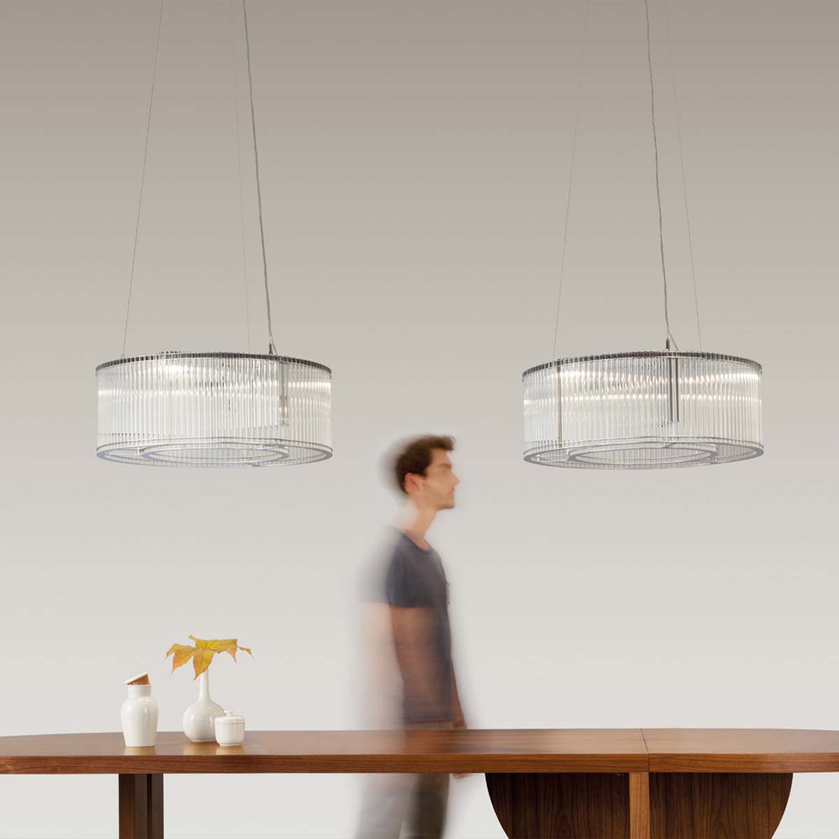 Zwei Pendelleuchten mit zylindrischem Glasschirm über einem Tisch hängend mit Person im Hintergrund