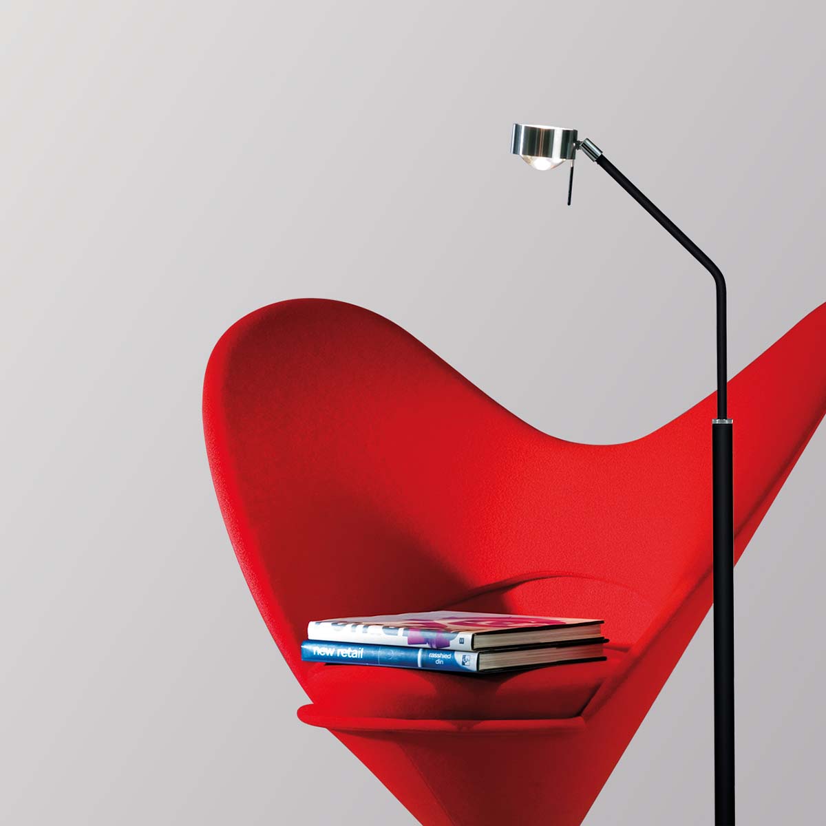 Schmale Stehleuchte in der Farbe chrom neben einem Stuhl stehend