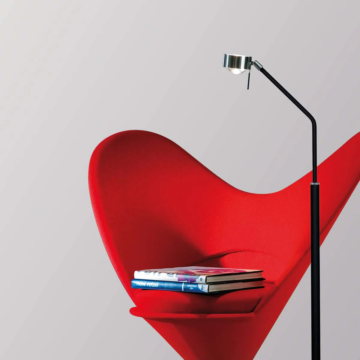 Schmale Stehleuchte in der Farbe chrom neben einem Stuhl stehend