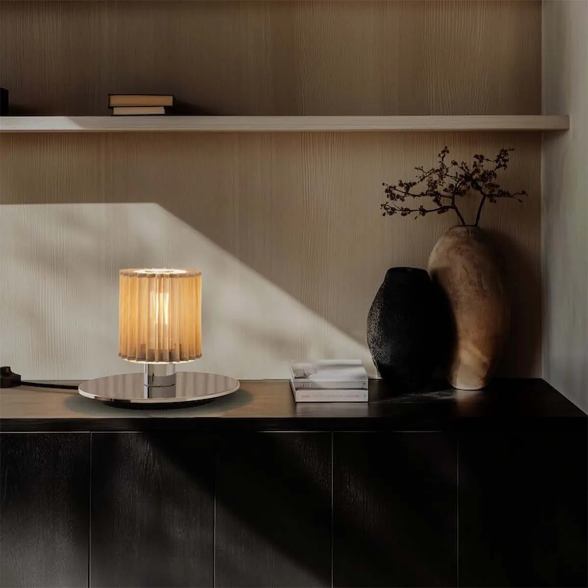 DCW Editions In The Sun Table 220 auf Sideboard – stilvolle Tischleuchte in Goldoptik auf dunklem Sideboard, harmonisch kombiniert mit Keramikvasen und sanftem Lichteinfall