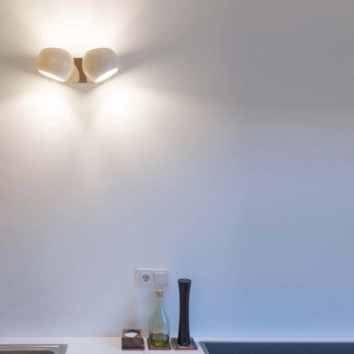 Doppelte Wandleuchte mit zwei weißen, asymmetrischen Lampenschirmen an der Wand in der Küche hängend