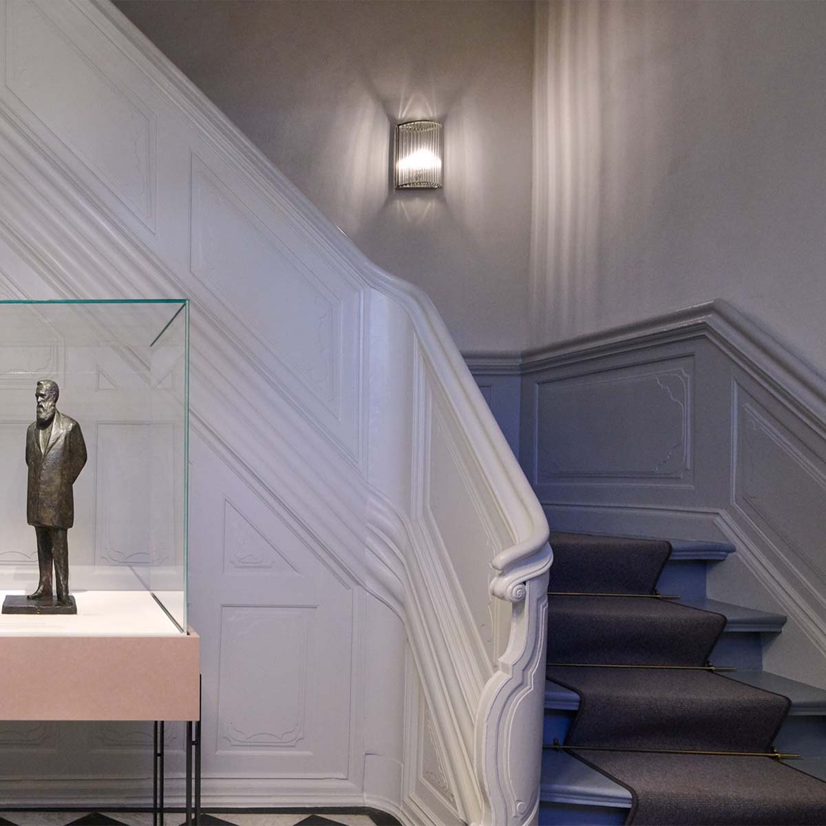 Elegante Wandleuchte mit zylindrischen Glasschirm im Flur bei der Treppe hängend