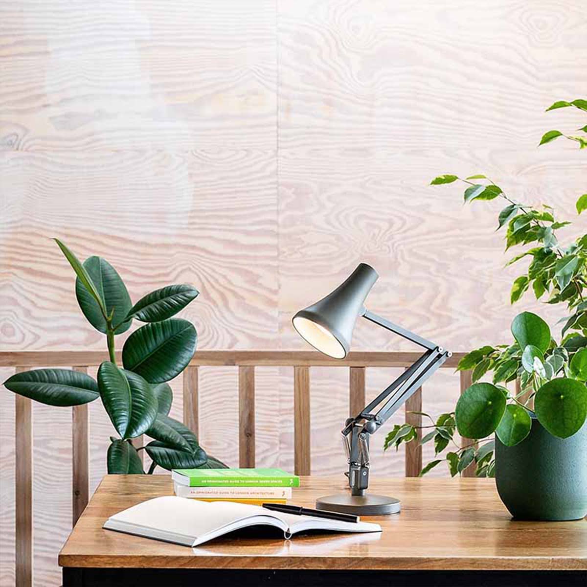 Graue Design-Tischleuchte auf Holztisch mit Pflanzen und Büchern, moderne Leselampe für Wohnzimmer oder Home Office