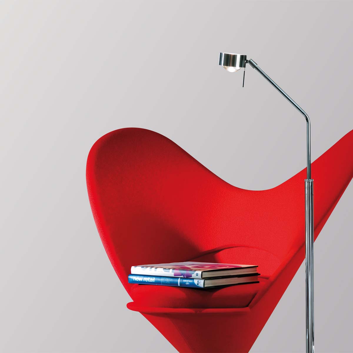 Schmale verchromte Stehleuchte neben einem Stuhl stehend