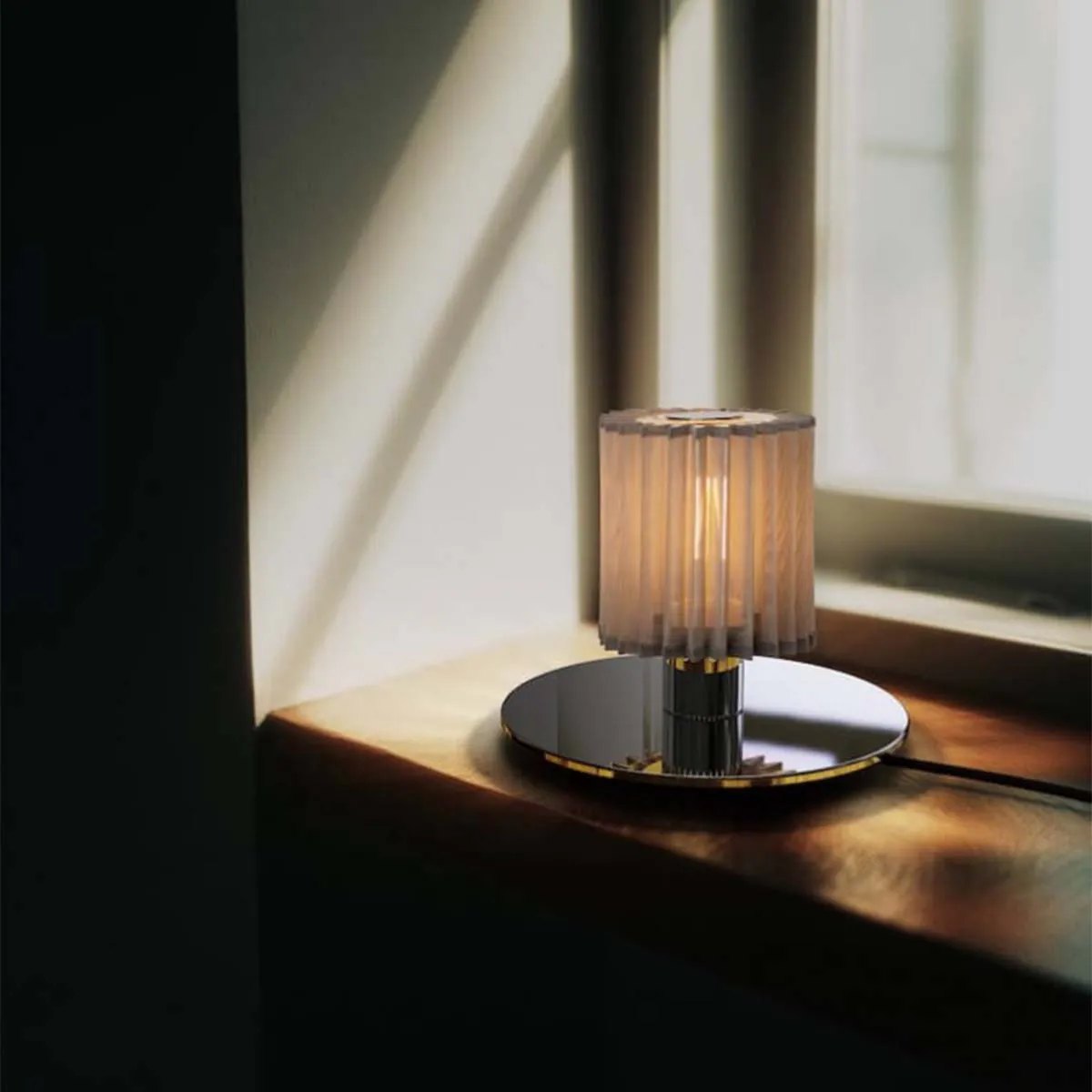 DCW Editions In The Sun Table 220 auf Schreibtisch – elegante Leuchte sorgt für warmes Licht auf einem hellen Schreibtisch mit geöffnetem Buch und natürlicher Dekoration