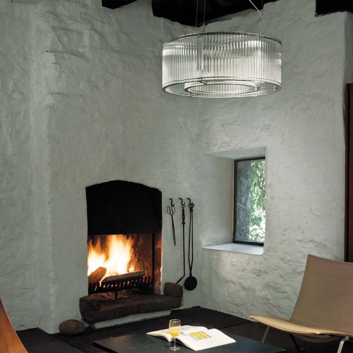 Elegante Pendelleuchte mit zylindrischen Glasschirm im Wohnzimmer neben einem Kamin hängend Elegante Pendelleuchte mit zylindrischen Glasschirm im Wohnzimmer neben einen Kamin hängend