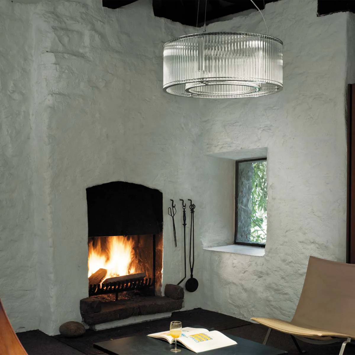 Elegante Pendelleuchte mit zylindrischen Glasschirm im Wohnzimmer neben einen Kamin hängend