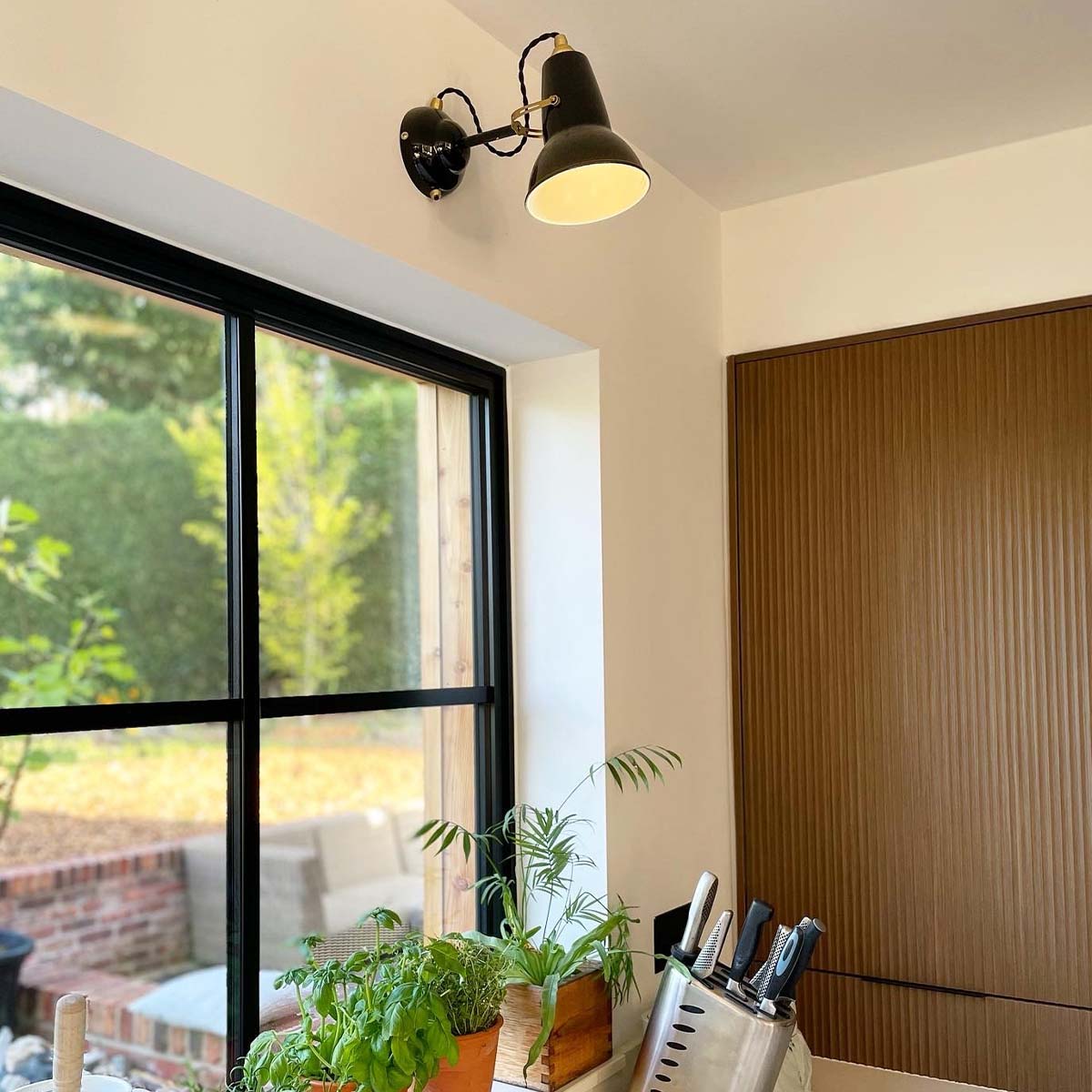 Anglepoise Original 1227 Wandleuchte, Ø: 13 cm, H: 16 cm im Wohnambiente: schwarze Design-Wandleuchte über Nachttisch in dunkelgrünem Schlafzimmer mit warmem Licht und dekorativen Details.