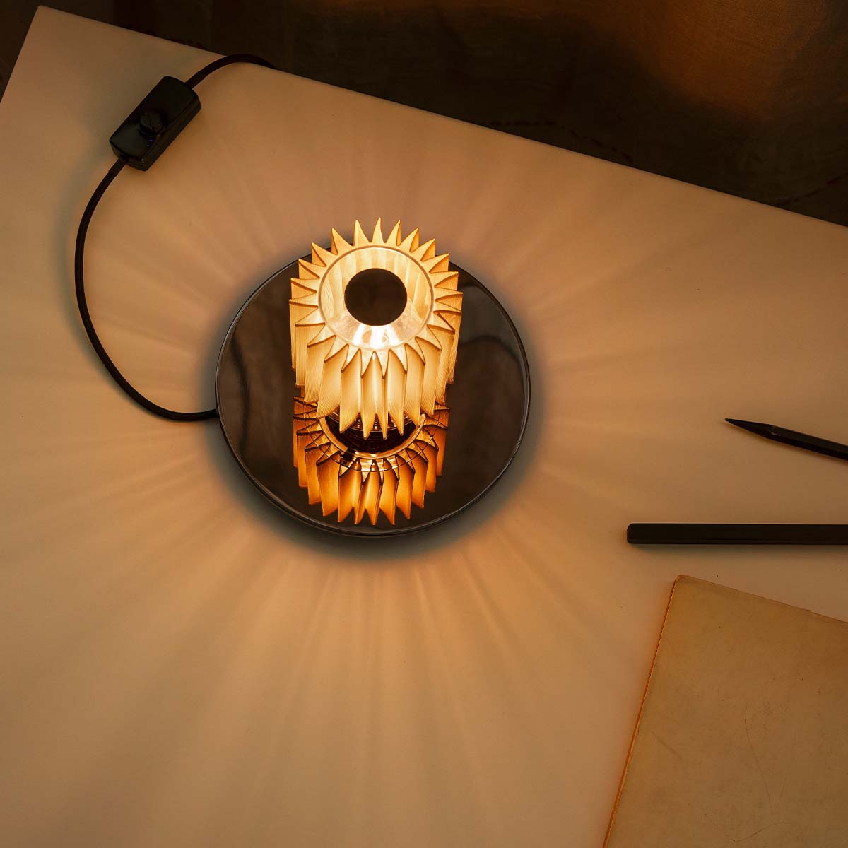 DCW Editions In The Sun Table 220 auf Schreibtisch – elegante Leuchte sorgt für warmes Licht auf einem hellen Schreibtisch mit geöffnetem Buch und natürlicher Dekoration