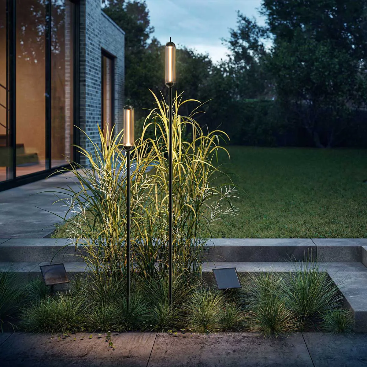 Zwei Stabförmige schwarze Erdspießleuchten mit Solarmodul und verbindungskabel im Beet im Garten