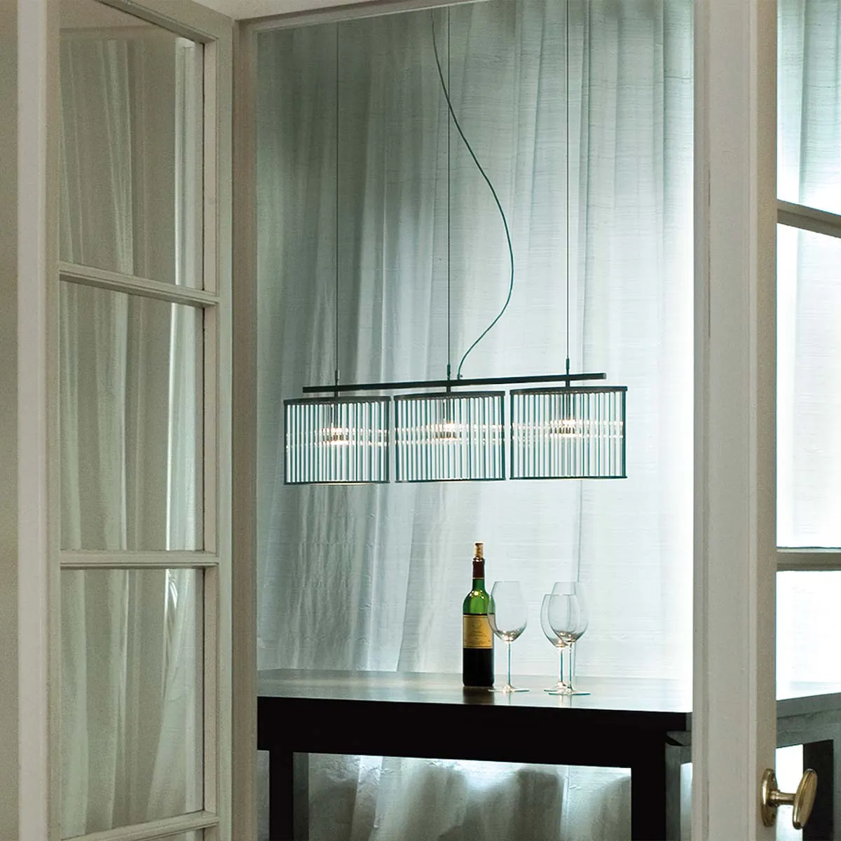 Moderne Pendelleuchte mit drei geschwungenen Glasschirmen über einen Esstisch hängend